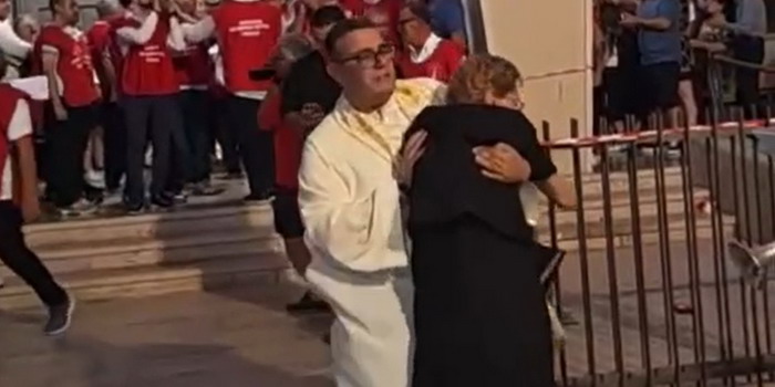 Il sacerdote solleva di peso un’anziana per metterla al riparo dai fuochi d’artificio durante i festeggiamenti di San Giovanni a Pozzallo